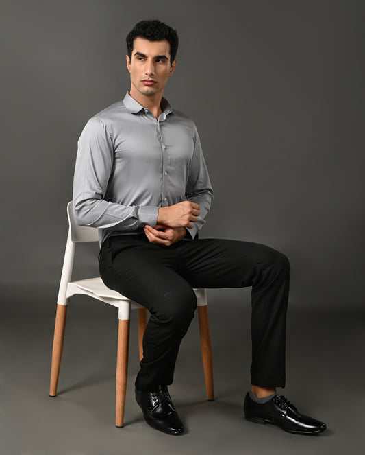 Man sitting on a chair wearing a light gray shirt and black pants against a gray background